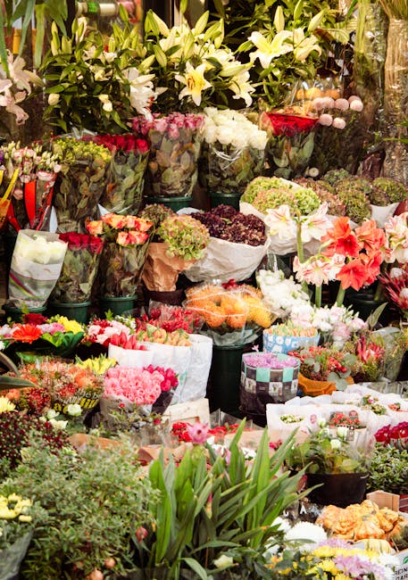 A vibrant display of fresh floral arrangements and bouquets at a flower market, featuring a variety of flowers including white lilies, pink roses, and multicolored carnations, wrapped in paper or pres